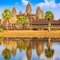 Historischer Tempel Angkor Wat in Kambodscha mit Palmen im Vordergrund und dramatischem Himmel im Hintergrund.
