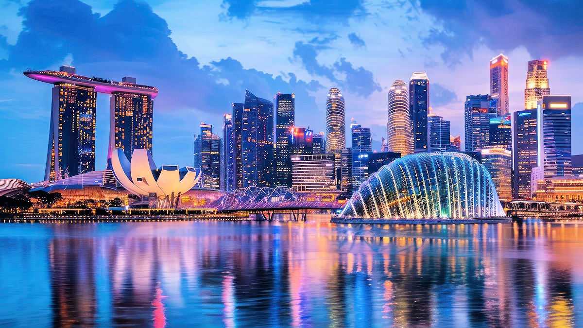 Kombireise Singapur: Beleuchtete Skyline von Singapur bei Nacht mit Marina Bay Sands und futuristischen Gebäuden, reflektiert im Wasser.